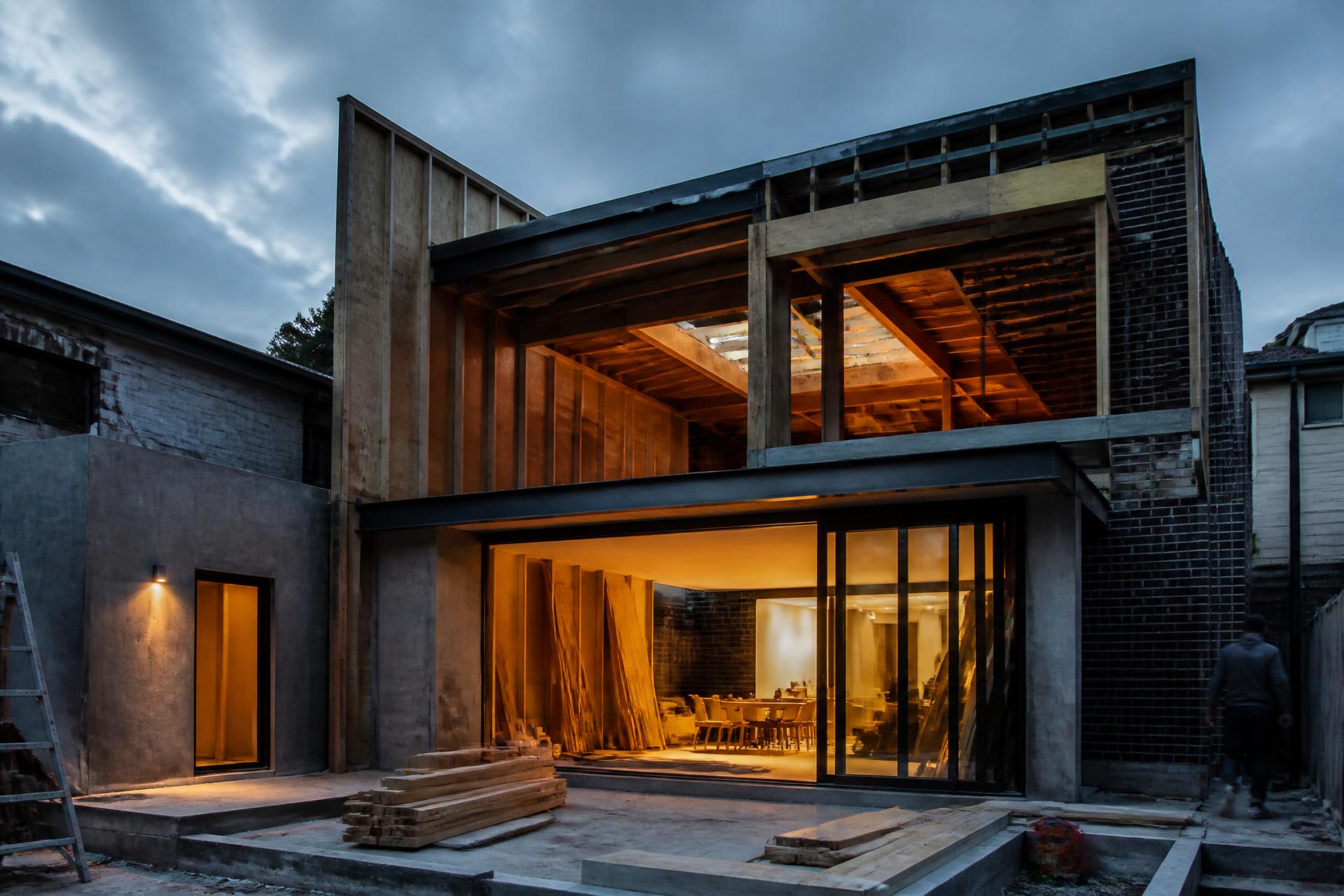 Rear extension under construction at dusk, with exposed timber framing and a fully glazed ground floor